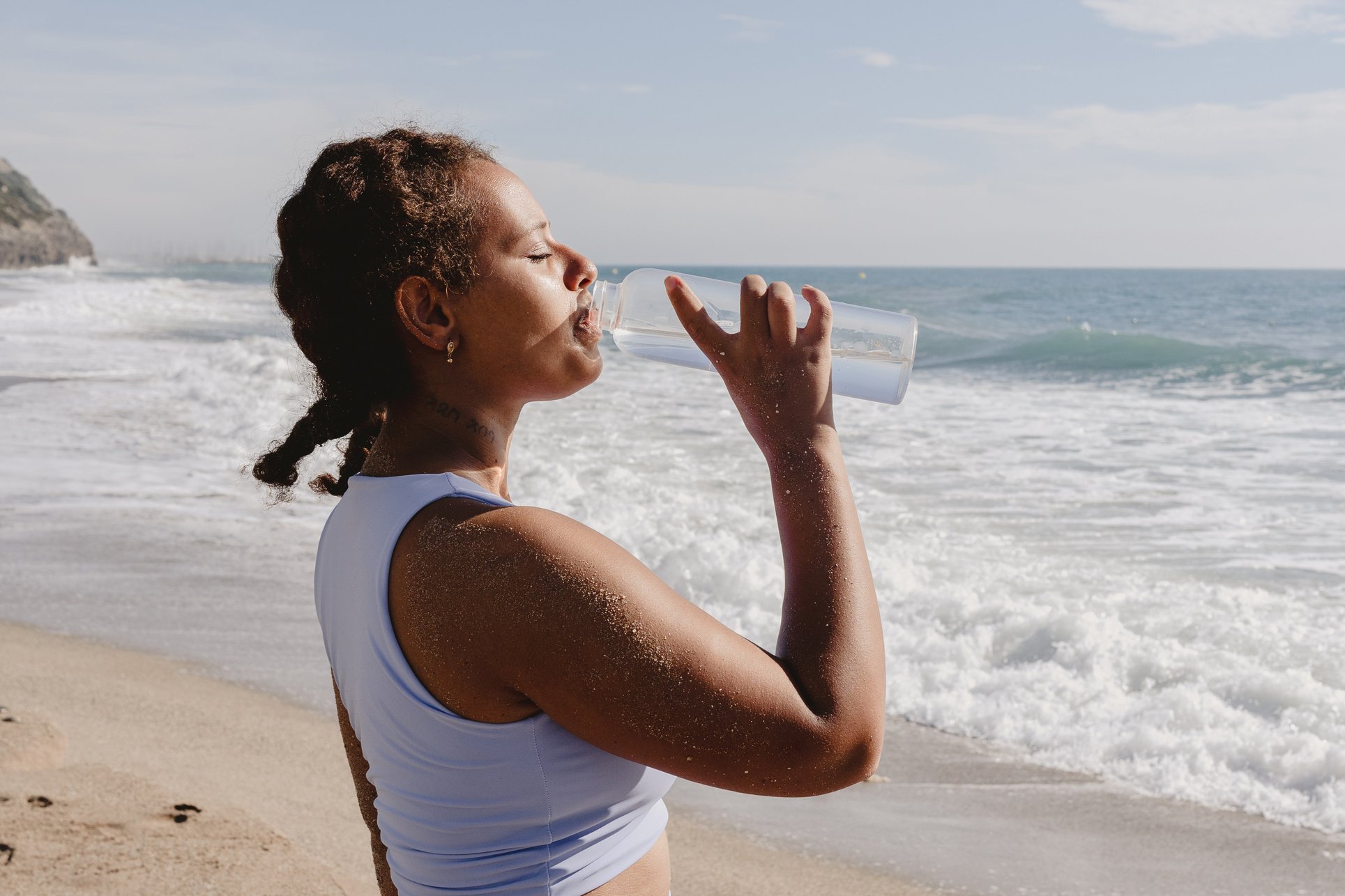 Woman Drinking Water from a Bottle by the Beach